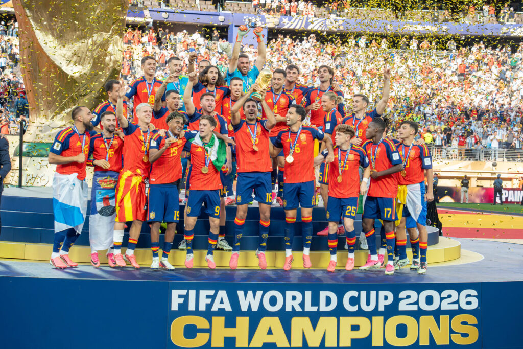 Jogadores da Espanha comemoram no palco com a taça da Copa do Mundo de 2026, sob chuva de confete, após vencer a Argentina na final