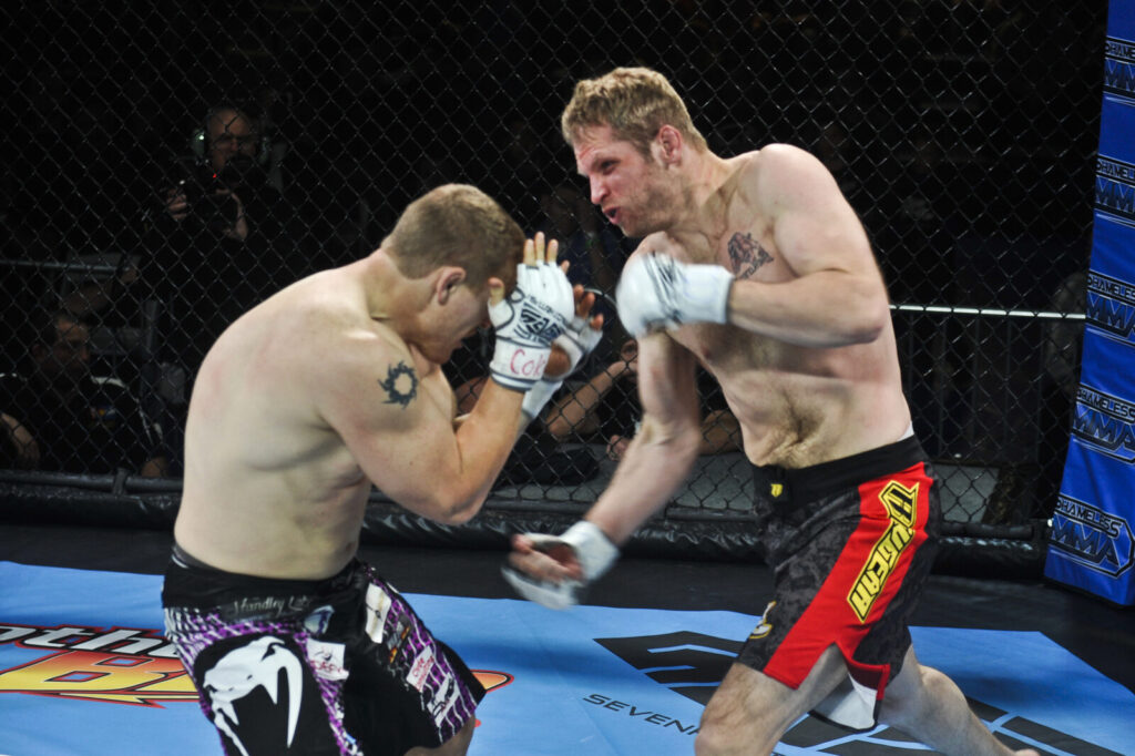 Dois lutadores de MMA trocam golpes dentro de um octógono, imagem ilustrativa de combate