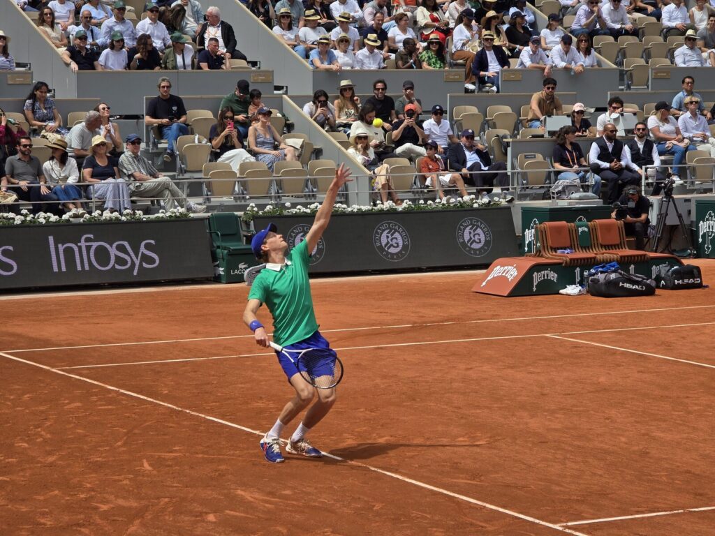 Jannik Sinner sacando durante partida de tênis em quadra de saibro