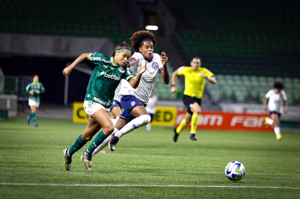 Duas jogadoras de futebol disputam a bola em campo durante partida do futebol feminino brasileiro