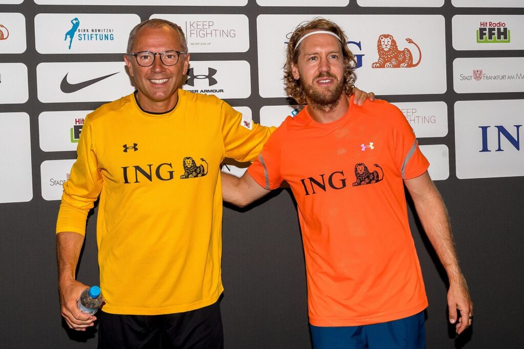 Stefano Domenicali, CEO da F1, sorrindo ao lado de Sebastian Vettel em evento beneficente (Foto de arquivo: Stefano Domenicali (CEO da F1) em evento beneficente de 2022, sem relação com uma corrida específica.)
