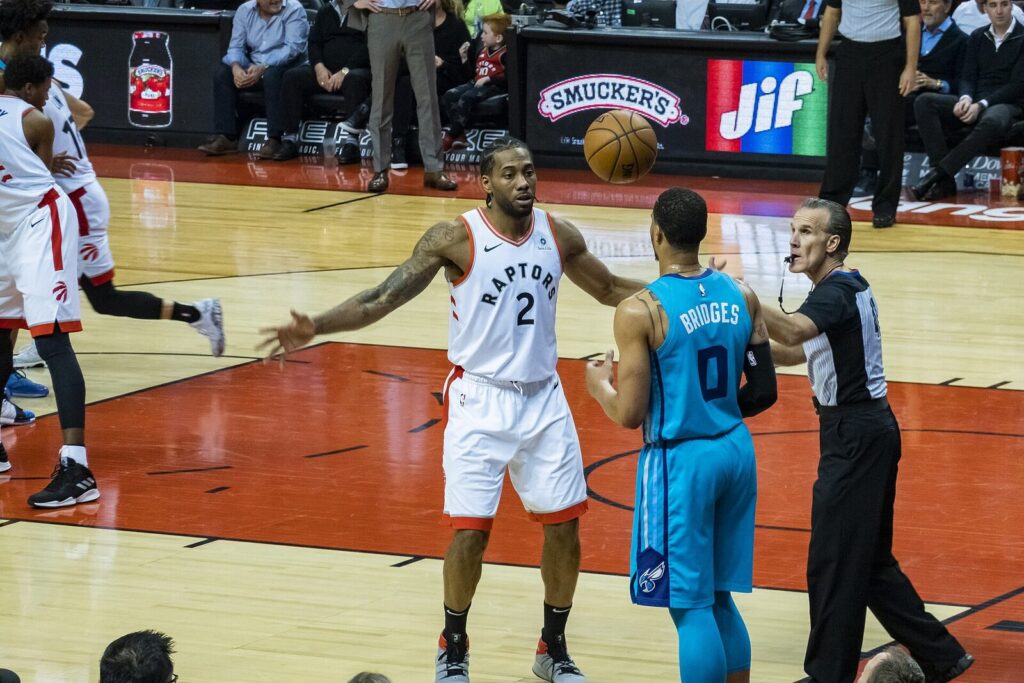 Kawhi Leonard com a camisa branca do Toronto Raptors disputa bola contra o Charlotte Hornets em 2019 (Foto de arquivo: Kawhi Leonard durante sua primeira passagem pelo Raptors, em 2019.)