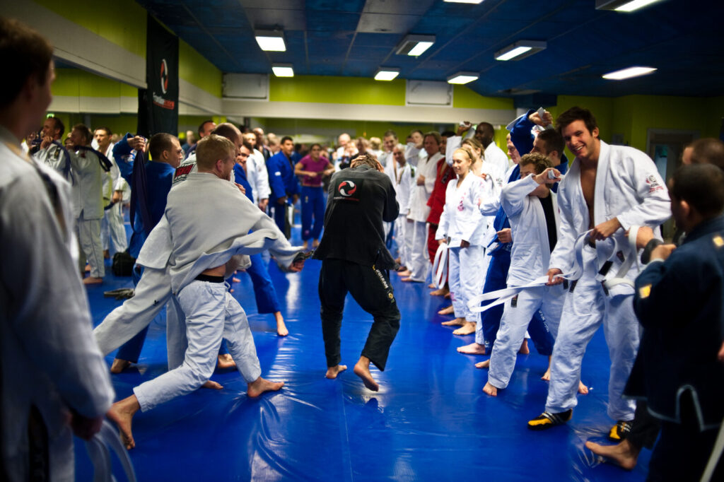 Cerimônia de passagem de faixa em Jiu-Jitsu ('corredor polonês'), com praticantes de faixas branca, azul e preta reunidos no tatame (Foto de arquivo: cerimônia de graduação de faixas em Jiu-Jitsu.)