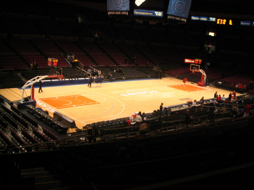 Vista elevada de quadra de basquete vazia e arquibancadas no Madison Square Garden, com placar visível (Foto de arquivo: quadra do Madison Square Garden em 2005, não do media day de 2026.)
