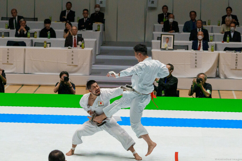Dois atletas de caratê em ação de kumite, vestindo kimonos brancos e cintos, durante disputa em tatame (Foto de arquivo: final de kumite masculino do JKA World Cup 2024, ilustrando praticantes de caratê e seus cintos.)