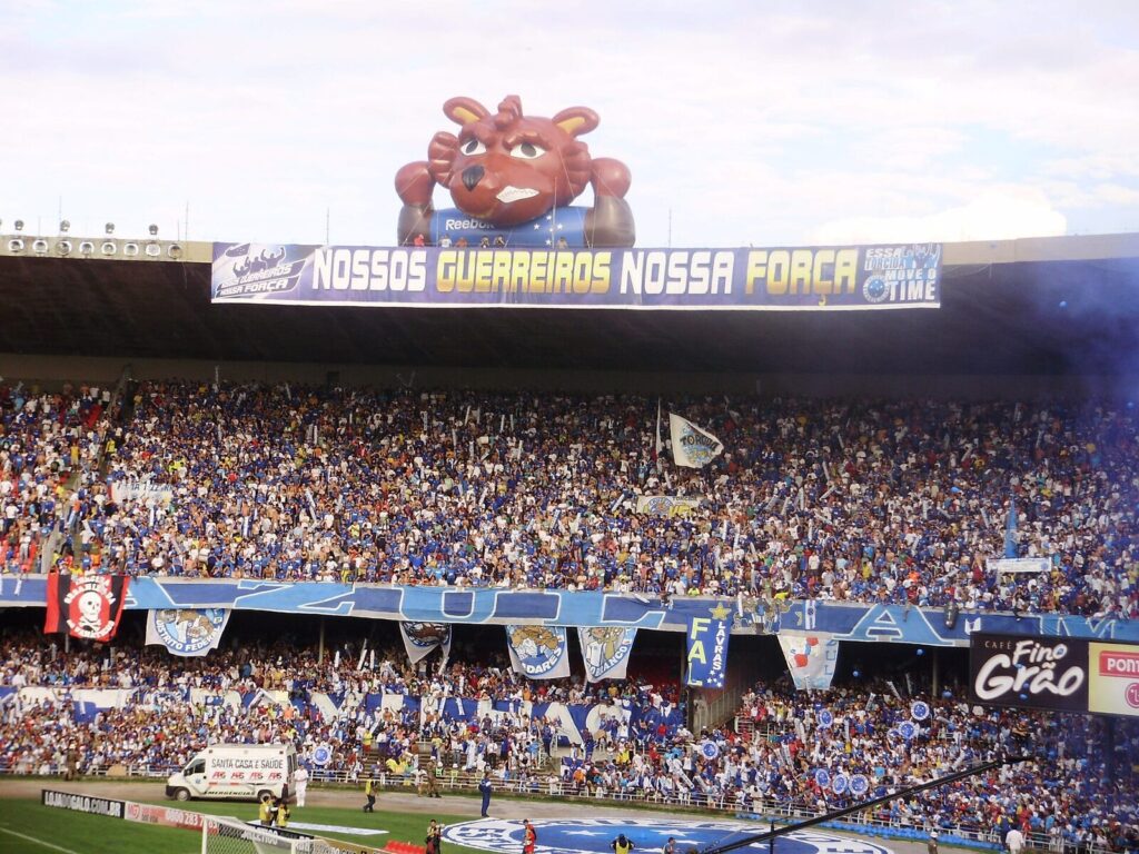 Torcida do Cruzeiro no Mineirão com mascote inflável da Raposa acima de faixa dos torcedores (Foto de arquivo: mascote inflável do Cruzeiro no Mineirão, torcida em jogo anterior.)