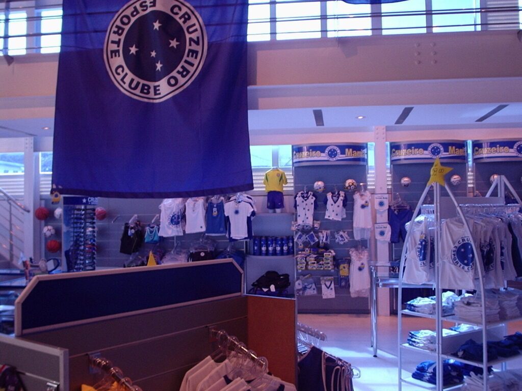 Interior da loja oficial do Cruzeiro em Belo Horizonte, com bandeira do clube, camisas e produtos à venda (Foto de arquivo: loja oficial do Cruzeiro, sem relação direta com a partida contra o Bragantino.)