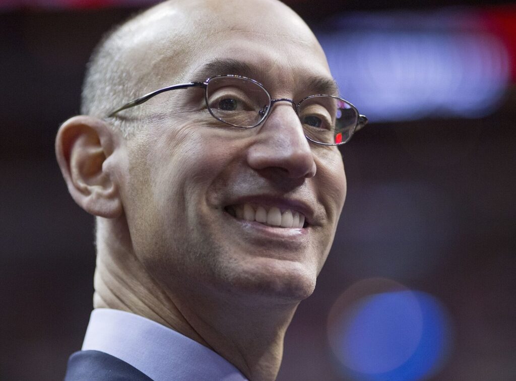 Retrato de perto de Adam Silver, comissário da NBA, sorrindo, usando óculos, em ambiente de arena (2014) (Foto de arquivo: Adam Silver, comissário da NBA, em 2014.)