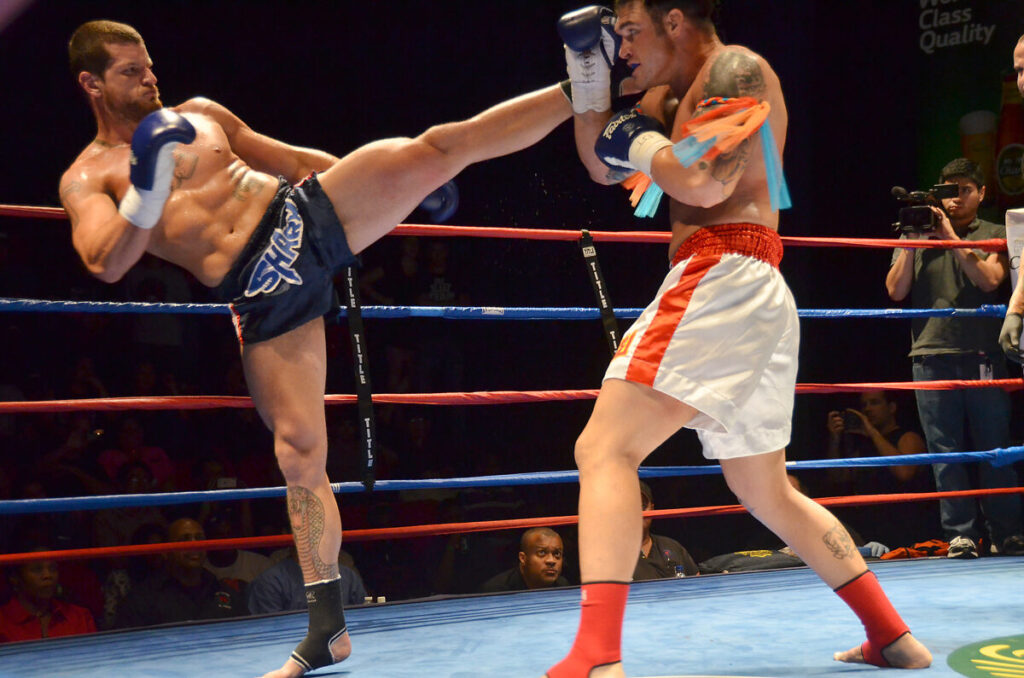 Lutador de muay thai aplica chute alto bloqueado pelo adversário em competição amadora (Foto de arquivo: luta de muay thai em competição amadora, sem relação direta com o sistema de graduação descrito na matéria.)