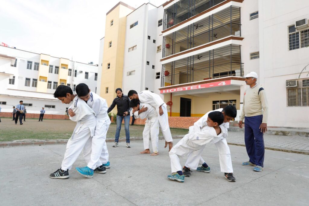 Grupo de jovens judocas com kimonos e faixas brancas praticando movimentos de judô ao ar livre (Foto de arquivo: prática escolar de judô, sem relação com evento específico.)