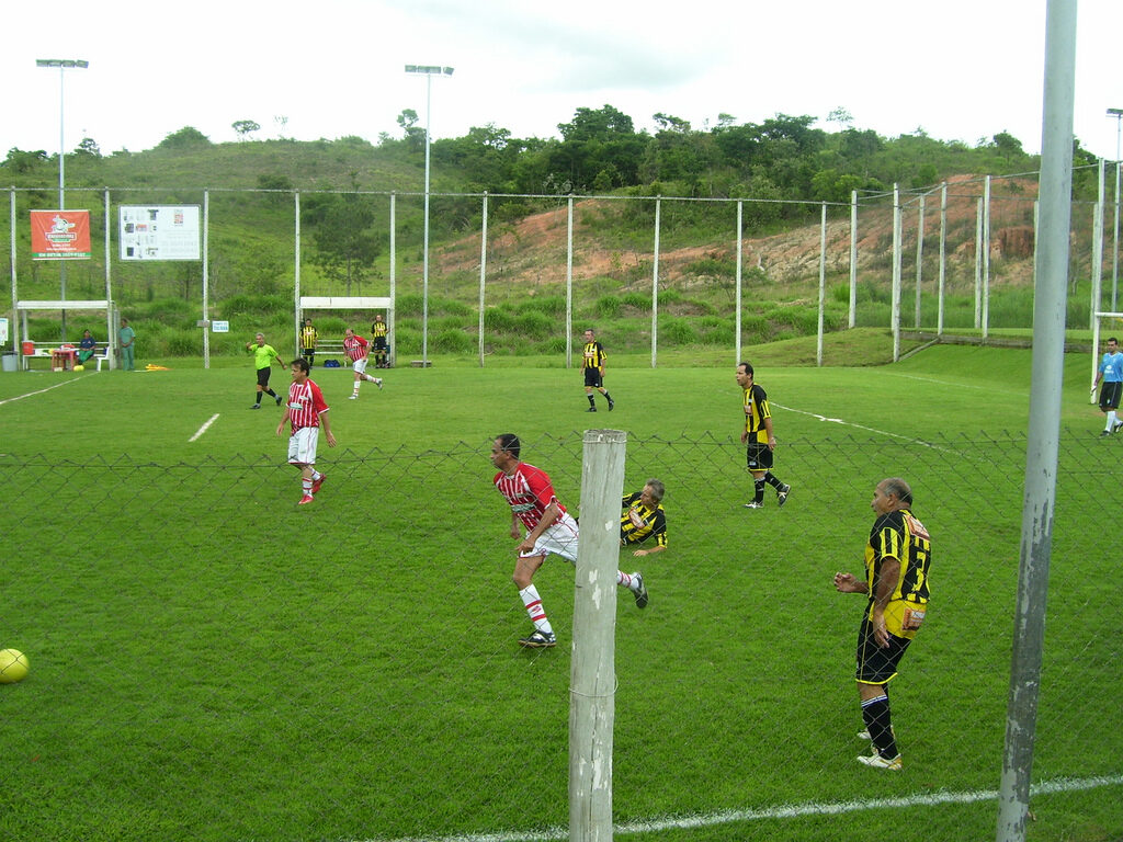 Partida de futebol society em campo sintético cercado por alambrado (Foto ilustrativa de uma partida de futebol society.)