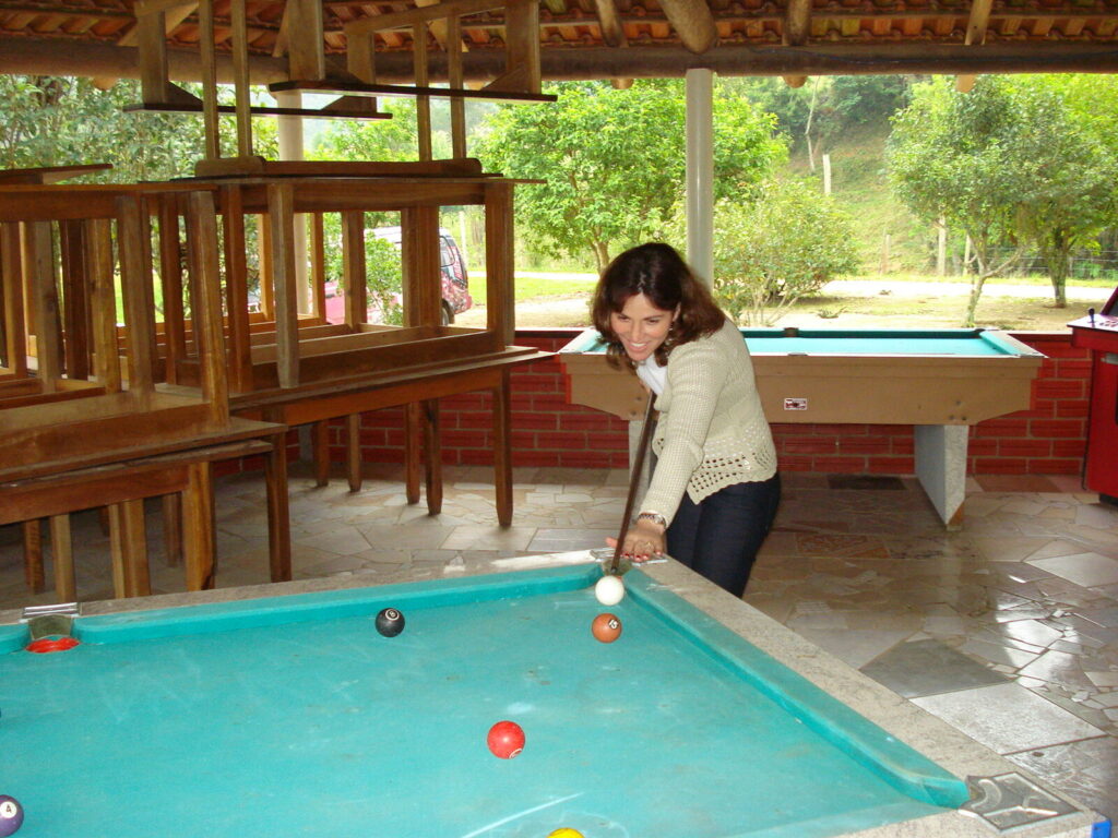 Mulher mirando uma tacada em mesa de sinuca ao ar livre, com a bola 8 visível sobre o pano (Foto de arquivo: partida amadora de sinuca.)